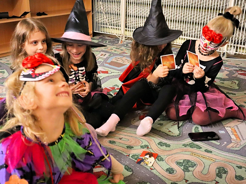 Piątka przebranych we wróżki dzieci siedzi na dywanie i gra w grę karcianą Dixi.