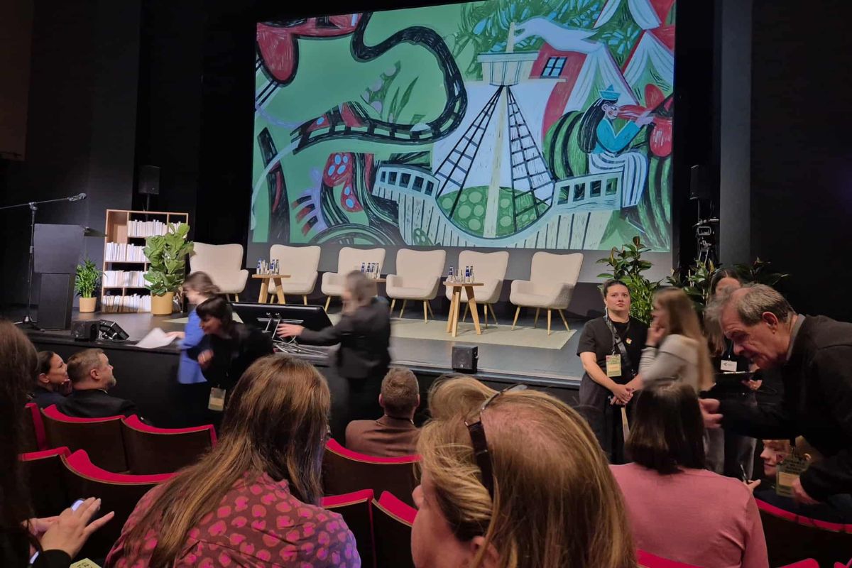Grupa ludzi w sali konferencyjnej, w tle ekran z kolorową ilustracją