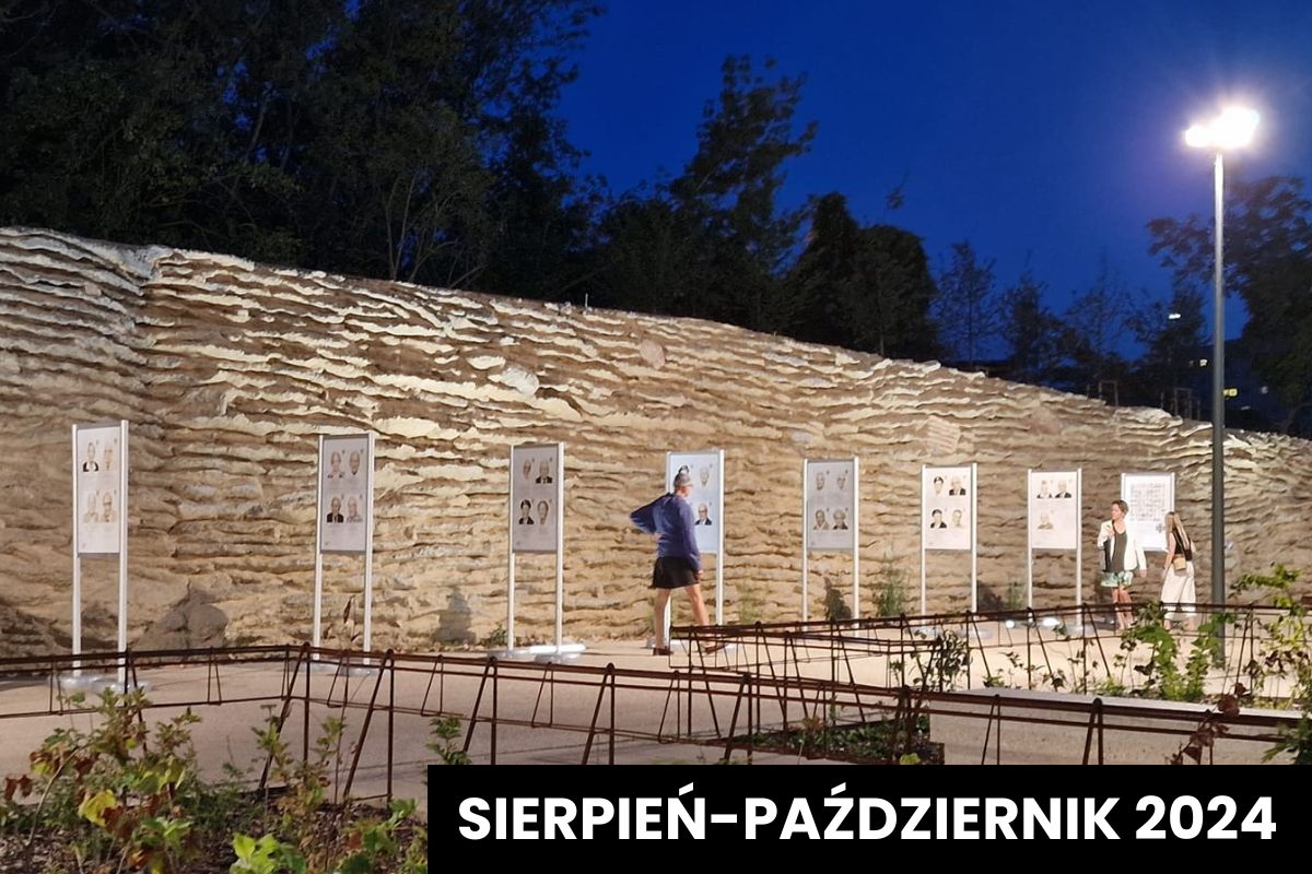 Widok na stojaki wystawowe, w tle mur, nocne niebo i latarnia
