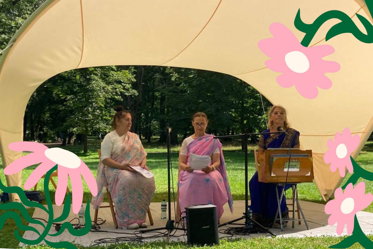 Trzy kobiety siedzą pod namiotem, śpiewają i grają na indyjskich instrumentach, po bokach ozdoby z różowych kwiatów