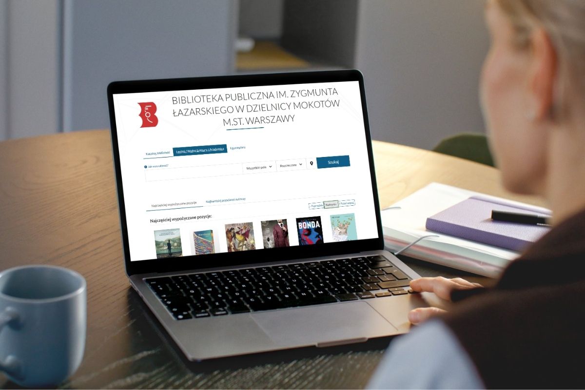 Kobieta siedzi przy komputerze i przegląda stronę Biblioteki Mokotów, z lewej błękitny kubek