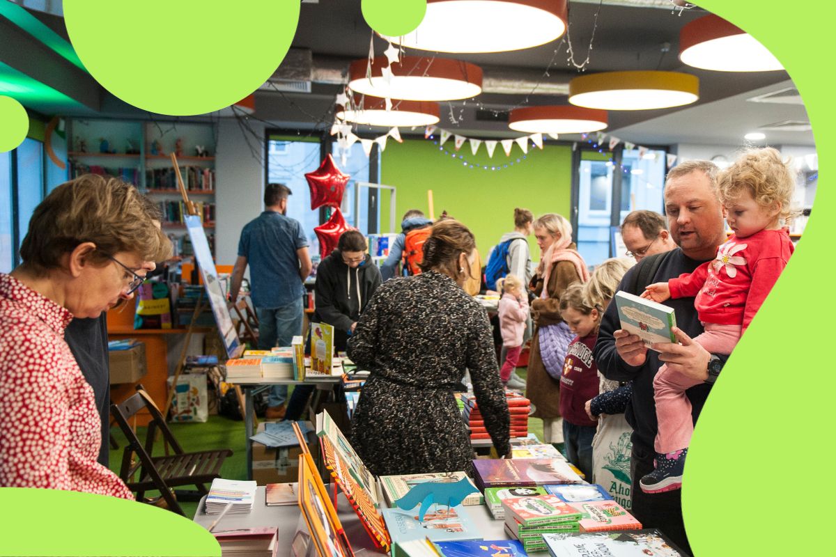 Ludzie przy stoiskach z książkami oglądają książki dla dzieci podczas kiermaszu