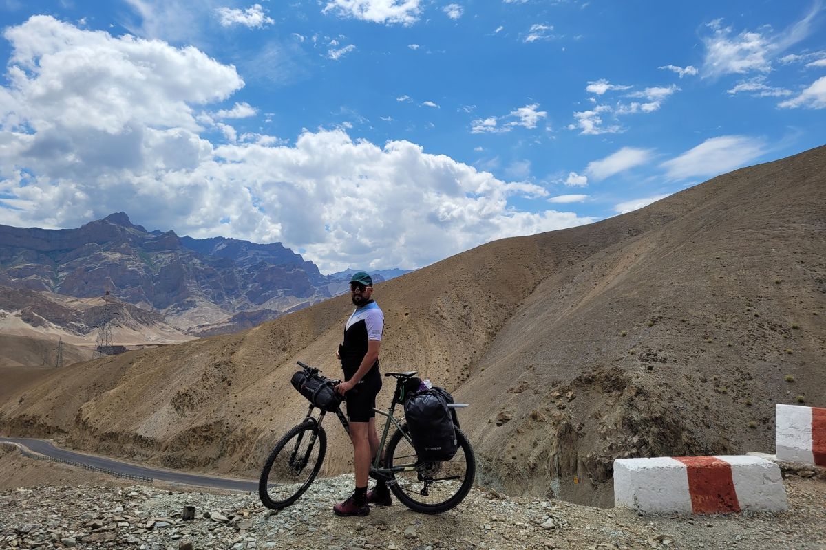 Mężczyzna stoi przy rowerze, w tle gór, błękit nieba, chmury