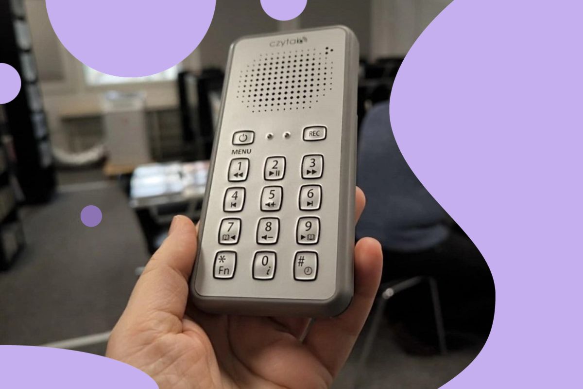 Ręka trzymająca czytak, po bokach fioletowe elementy ozdobne