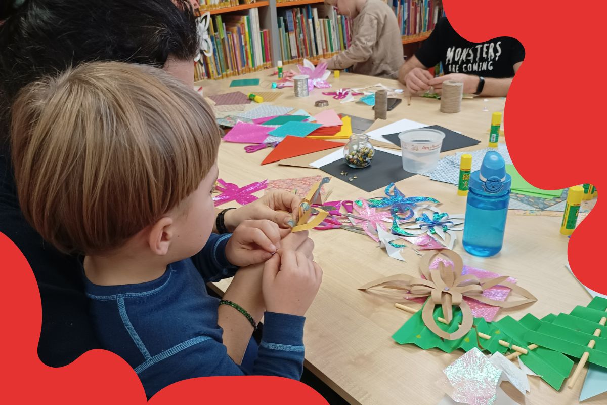 Chłopiec razem z mamą wykonują świąteczne ozdoby w bibliotece, czerwone elementy graficzne
