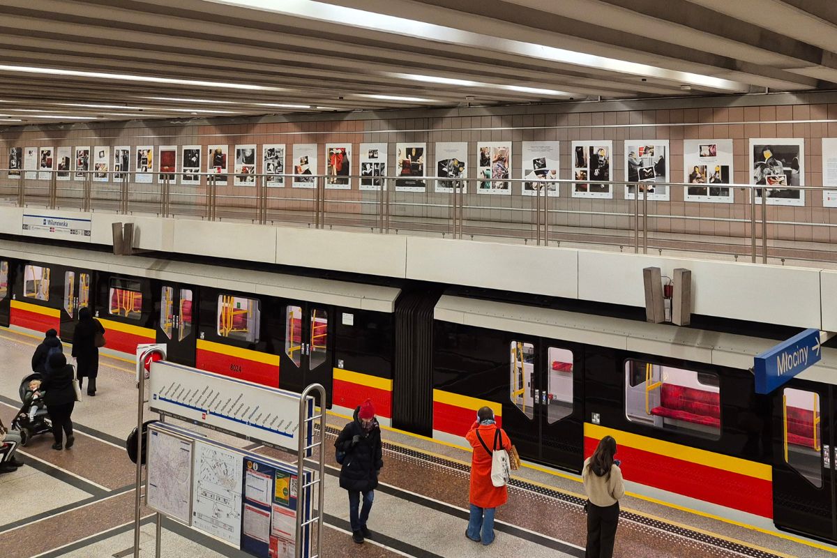 Perona na stacji metra, pociąg, pasażerowie, w tle antresola z planszami wystawy
