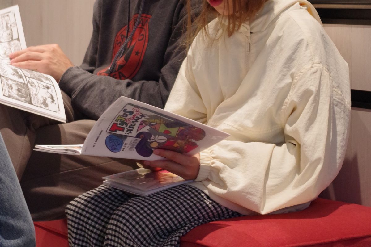 Młoda osoba siedzi na czerwonej kanapie i czyta komiks