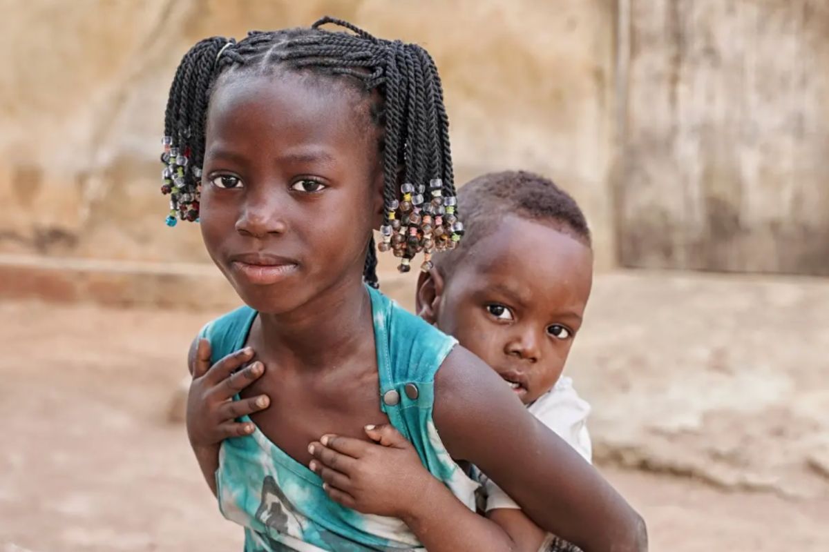 Dwoje dzieci o czarnej skórze, chłopczyk na plecach dziewczynki, w tle skały