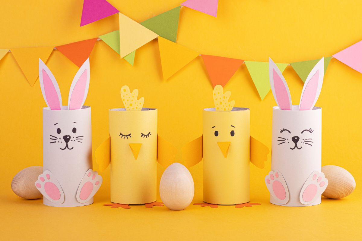 Na żółtym tle zajączki i kurczaczki z rolek po papierze toaletowym, kolorowa girlanda i drewniane jajka