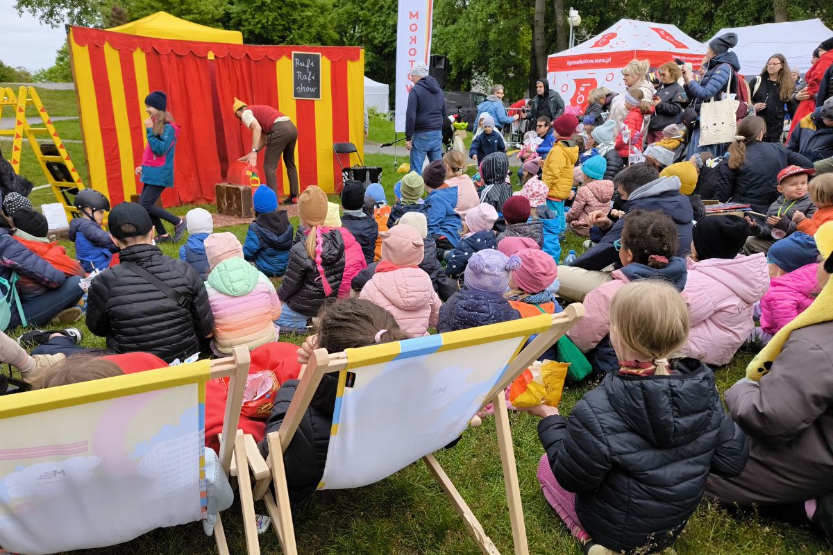 Grupa dzieci i dorosłych podczas pikniku ogląda przedstawienie z klaunem