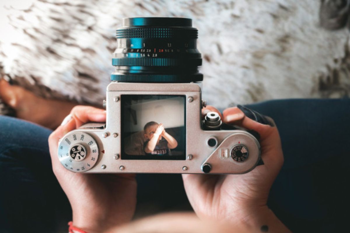 Ręce trzymające analogowy aparat fotograficzny, w jego kadrze dziecko