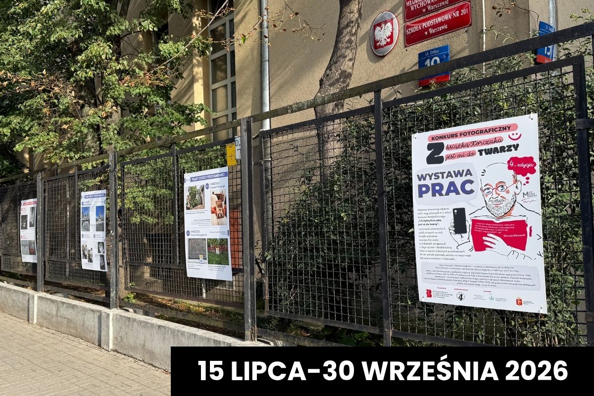 Plansze z wystawą pokonkursową przypięte do ogrodzenia, w tle budynek szkoły i drzewa