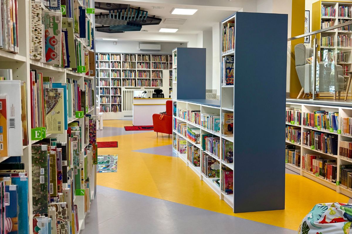 Wnętrze biblioteki dla dzieci, regały z książkami, worek sako, w głębi lada biblioteczna, czerwony fotel