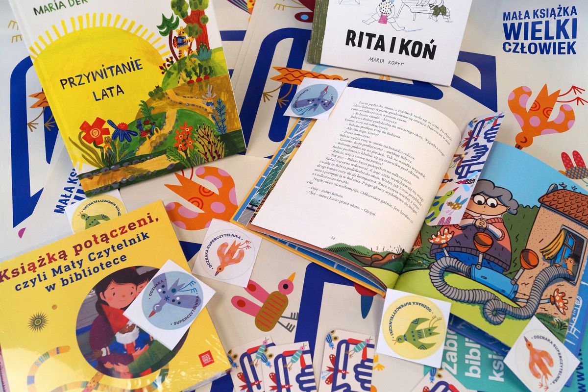 Zestaw materiałów projektu – otwarte książki, naklejki i plakaty – rozłożony na płaskiej powierzchni.