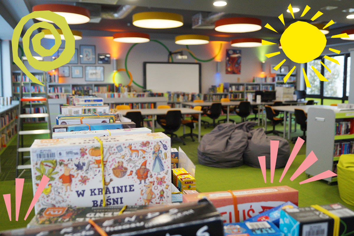 Nastolatka siedzi przy stole w bibliotece, pracuje na laptopie i uśmiecha się. Wokół niej leżą otwarte książki, a za nią widać regały z książkami.