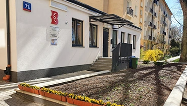Budynek biblioteki otoczony zielonymi drzewami. Słoneczna aura.
