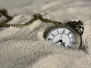 Na zdjęciu widoczny zegarek kieszonkowy leżący na piachu