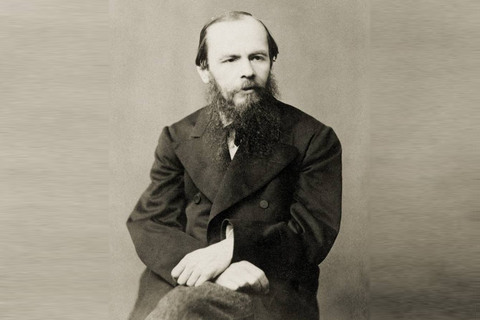 Dostojewski pozuje do czarno-białej fotografii na siedząco. Twarz czterdziestolatka, z dużymi zakolami i długą, rzadką brodą i wąsami. Ubrany w ciemny płaszcz. Ręce założone jedna na drugą.