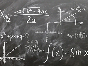 Na zdjęciu szara tablica z równaniami matematycznymi.