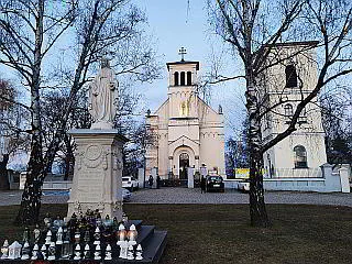 Kościół św. Katarzyny na warszawskim Służewie wraz z figurą Matki Boskiej Nieustającej Pomocy na pierwszym planie. Wokół cokołu figury, stojącego na trawniku, znajdują się zapalone znicze. Po obydwu stronach figury znajdują się dwie brzozy. Po prawej stronie kościoła znajduje się dzwonnica.