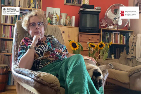Poetka siedzi w fotelu, obok niej leży nieduży piesek. W tle znajdują się regały z książkami oraz dwie szafki. Na szafkach stoją ozdobne, gliniane wazony oraz mały telewizor. Poniżej ich widać czubki czterech dojrzałych słoneczników. Autorka ma krótką, jasną fryzurę, okulary, a na prawej ręce bransoletę z zielonym kamieniem. Ubrana jest w kolorową bluzę i długą, zieloną spódnicę.