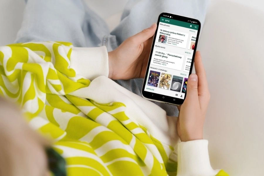 Kobieta trzyma w ręku smartfon z włączoną aplikacją biblioteczną