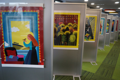 Plansze z ilustracjami Marianny Oklejak stoją wyeksponowane w sali bibliotecznej. Ilustracje przedstawiają różne wizerunki Maryi.