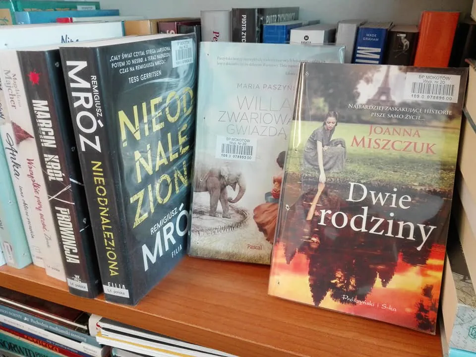 Kilka książek stoi na półce i przodem okładka książki Dwie rodziny.