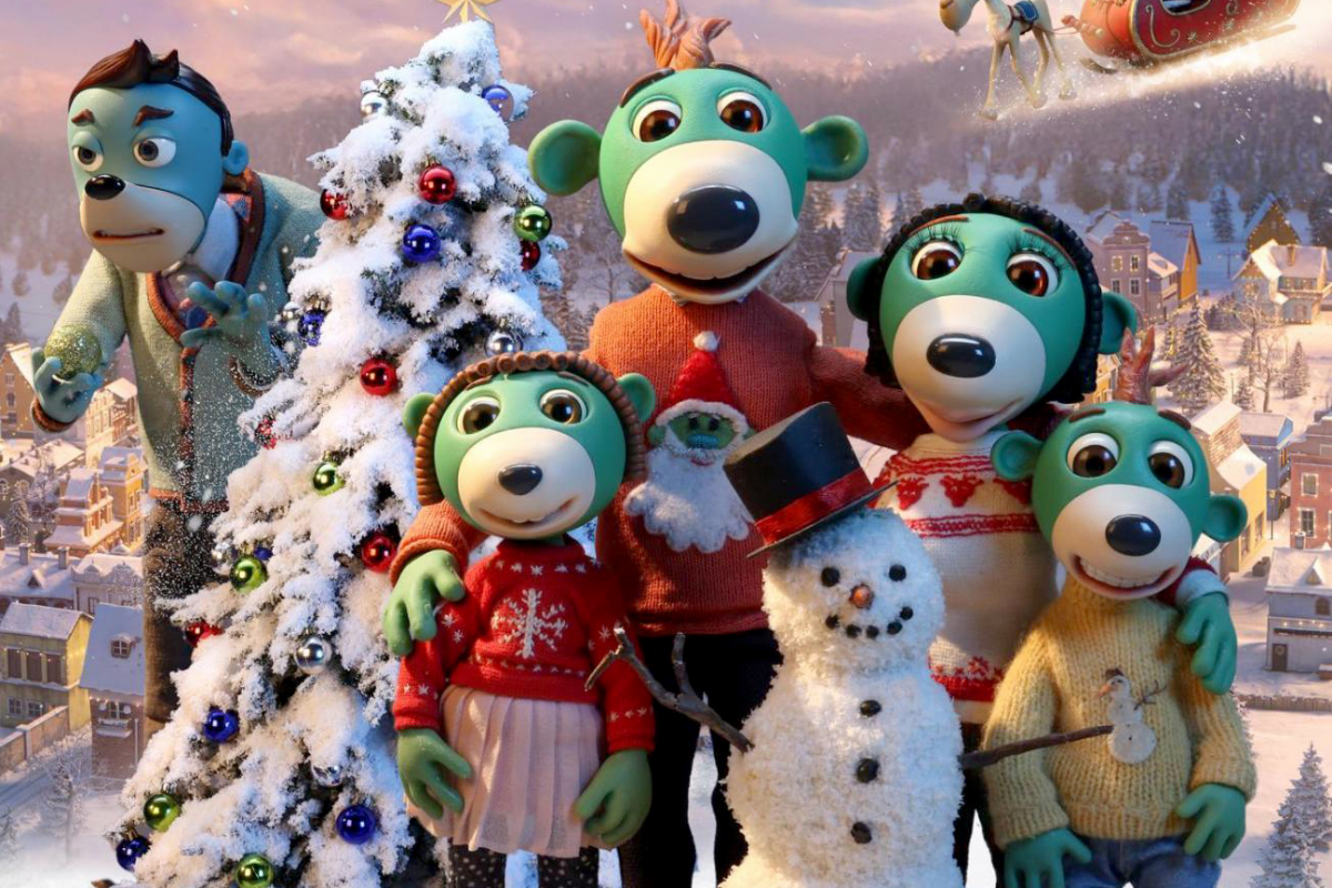 Grupa bajkowych postaci o zielonych pyszczkach i dużych oczach pozuje zimą przed ośnieżoną choinką. Ubrane w kolorowe swetry, stoją obok bałwana z cylindrem. W tle widać zimowe miasteczko i lecące sanie Świętego Mikołaja