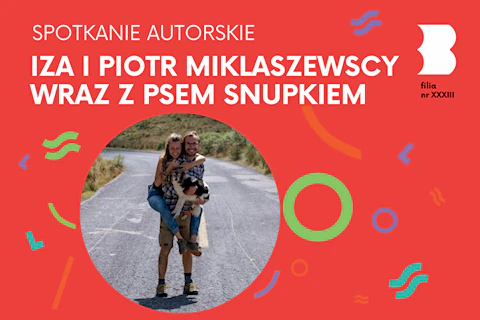 Na asfaltowej drodze otoczonej zielenią stoi brodaty mężczyzna w rękach trzymając psa, a na plecach mając uwieszoną kobietę.
