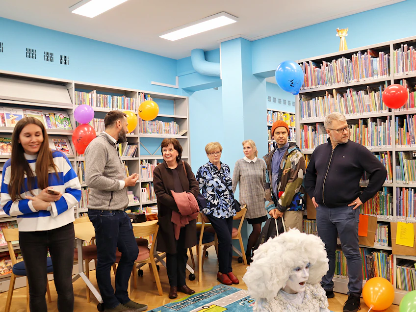 Grupa dorosłych osób rozgląda się wokół po pomieszczeniu bibliotecznym.