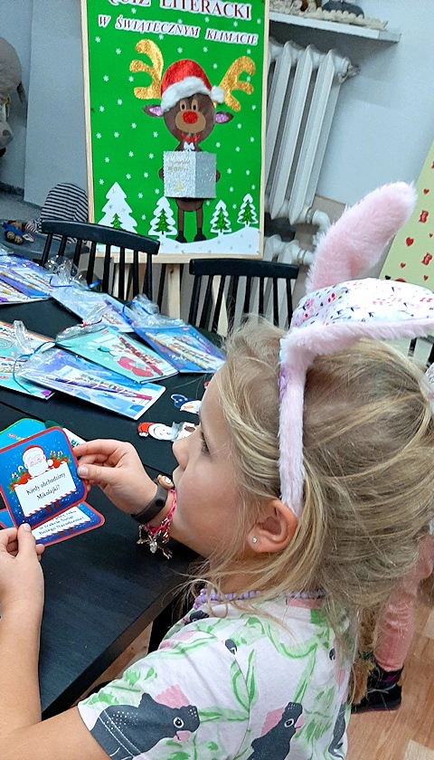 Blond dziewczynka z opaską z króliczymi uszami trzyma kartę ze świątecznym quizem w ręku.