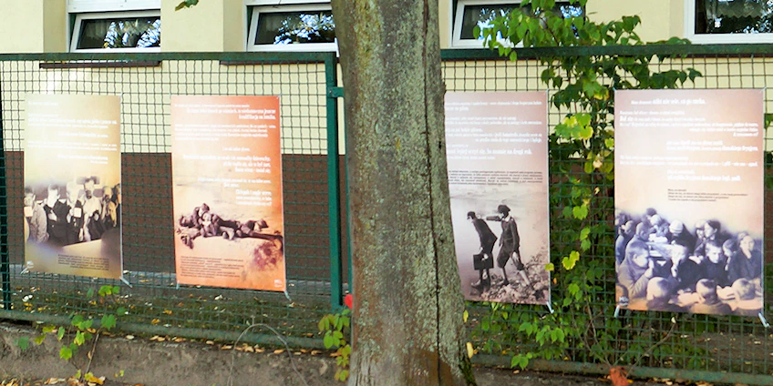 Cztery plansze powieszone na drucianym, zielonym płocie. Na wszystkich poza nieczytelnym tekstem zdjęcia małoletnich dzieci.
