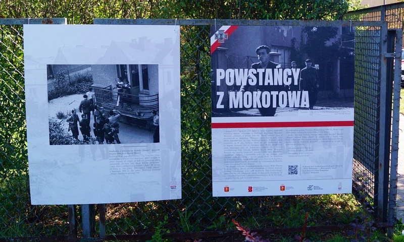 Dwie plansze ze zdjęciami i tekstem powieszone na drucianym płocie. Na prawej wyraźny napis: powstańcy z Mokotowa.