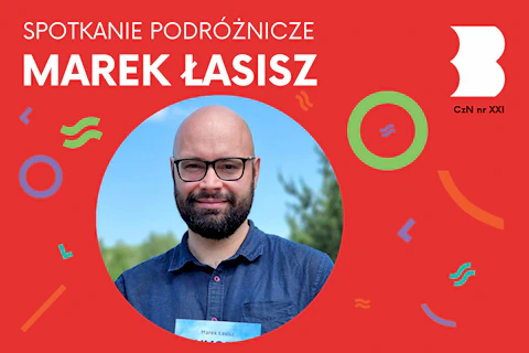 Młody, brodaty, łysy mężczyzna w okularach w granatowej koszuli na tle lasu i nieba.
