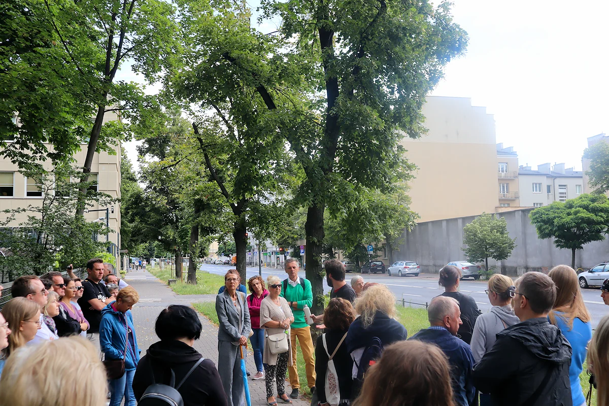 Grupa ludzi zgromadzona wokół przewodnika na ulicy Rakowieckiej przy byłym areszcie śledczym.