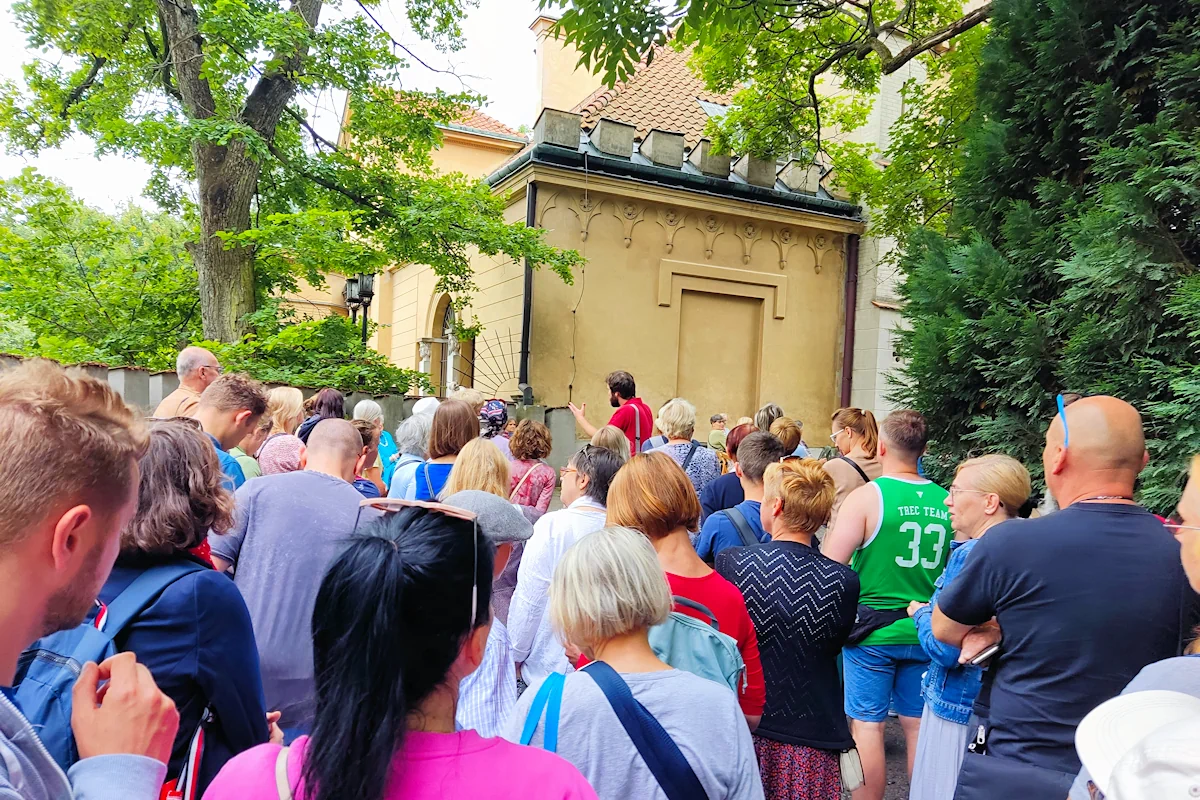 Dywan głów jest skierowanych na fragment historycznego budynku, chyba w stylu klasycznym. Z prawej i lewej fragmenty dwóch drzew.