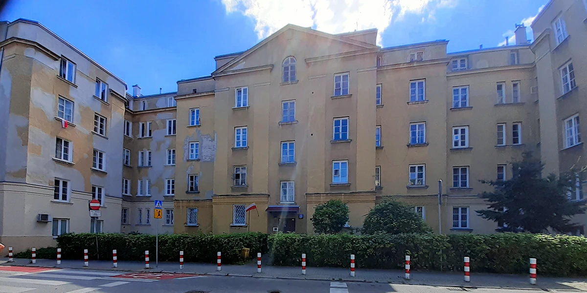 Trzypiętrowy budynek przedwojenny o żółtych ścianach z białymi plamami zaniedbania. Centralna część jest wcięta. Skrzydła budynku mają głębokość dwóch okien.