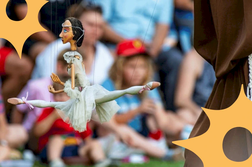 Marionetka baletnicy na tle rozmazanej publiczności.