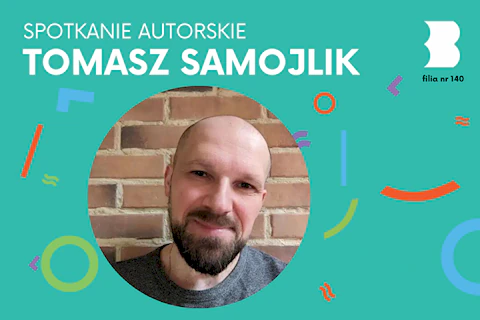 Łysawy mężczyzna z brodą i wąsami uśmiecha się serdecznie do obiektywu.