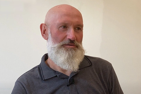 Na zdjęciu Marek Dąbrowski na tle beżowej ściany.