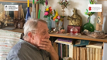 Mężczyzna, Piotr Wojciechowski, w swoim pokoju. Na ścianach obrazy, dekoracje na komodzie.