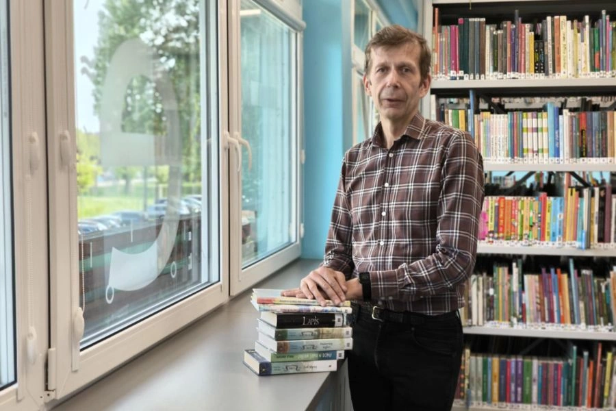Mężczyzna stoi przy oknie w bibliotece, na parapecie leżą książki
