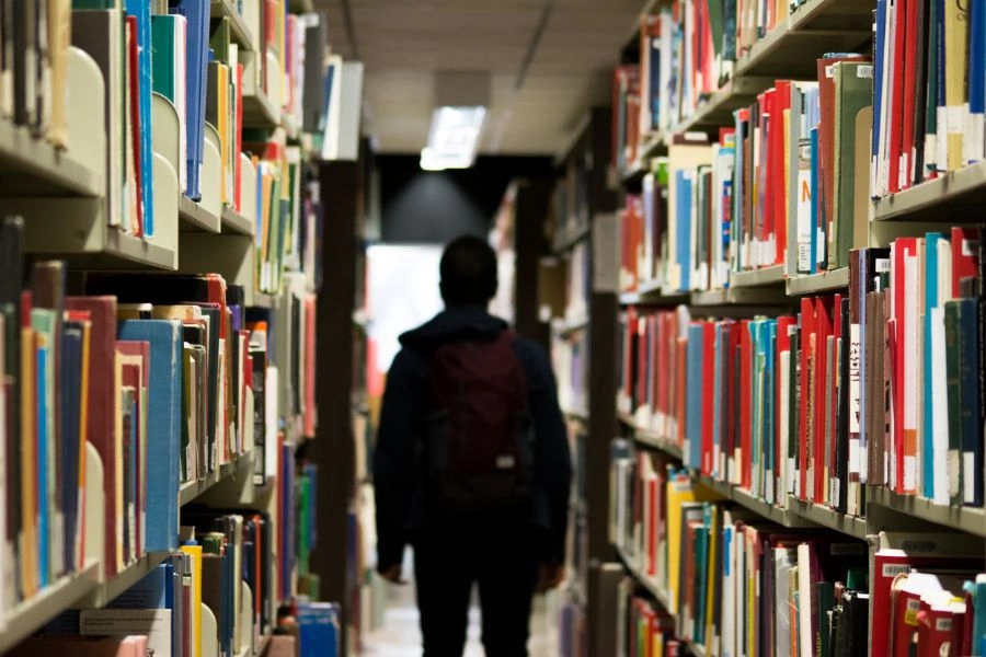 Sylwetka człowieka od tyłu pomiędzy regałami w bibliotece