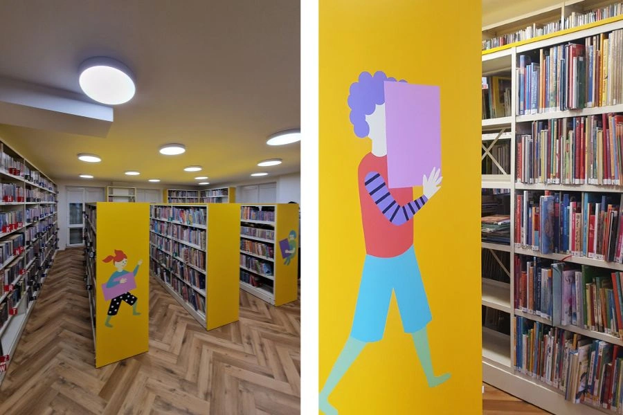 Wnętrza biblioteki, regały z książkami, naklejka czytającego chłopca na boku regału