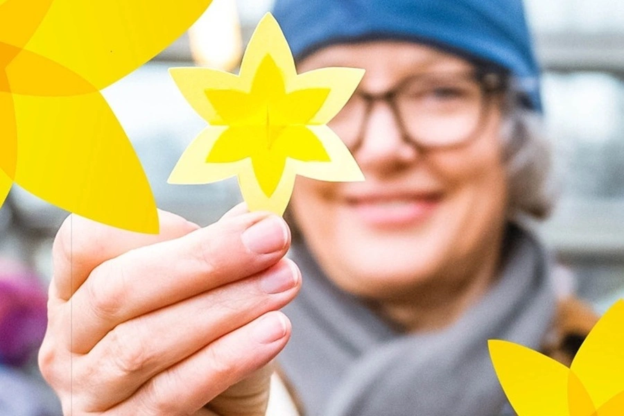 Kobieta w niebieskiej czapce trzyma przed oczami papierowego żonkila