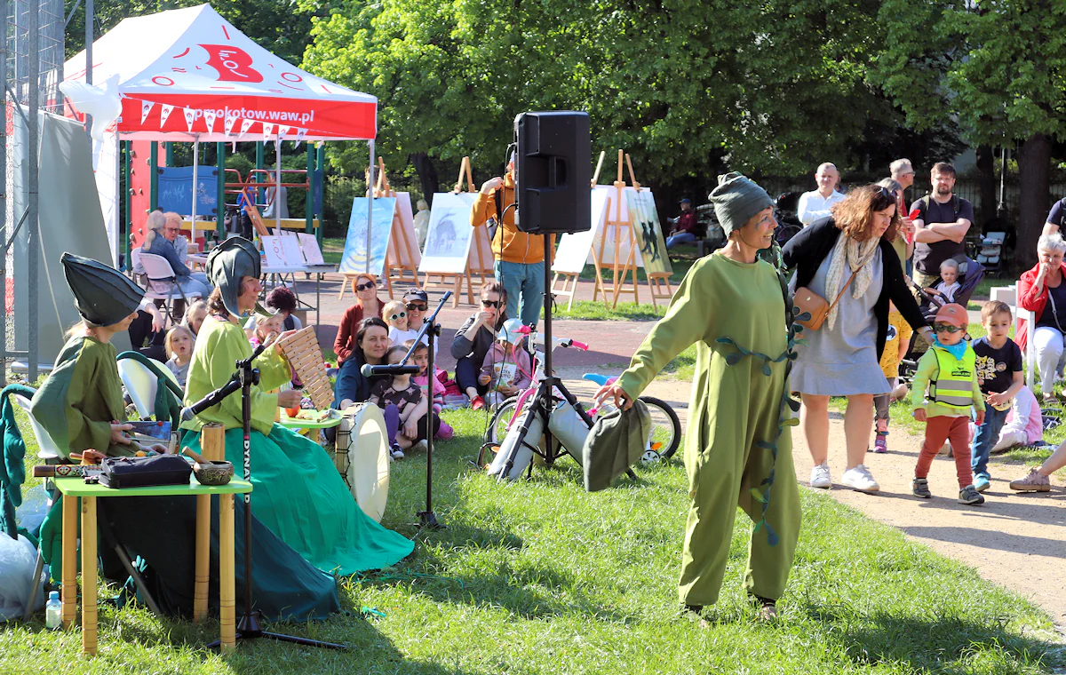 Trójka aktorek ubranych w zielone stroje zabawia na pikniku publiczność niewidoczną w kadrze.