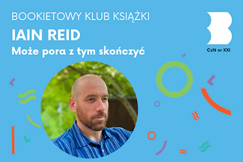 Łysy mężczyzna z rudym zarostem w niebieskiej koszuli patrzy na prawo zamyślonym wzrokiem.